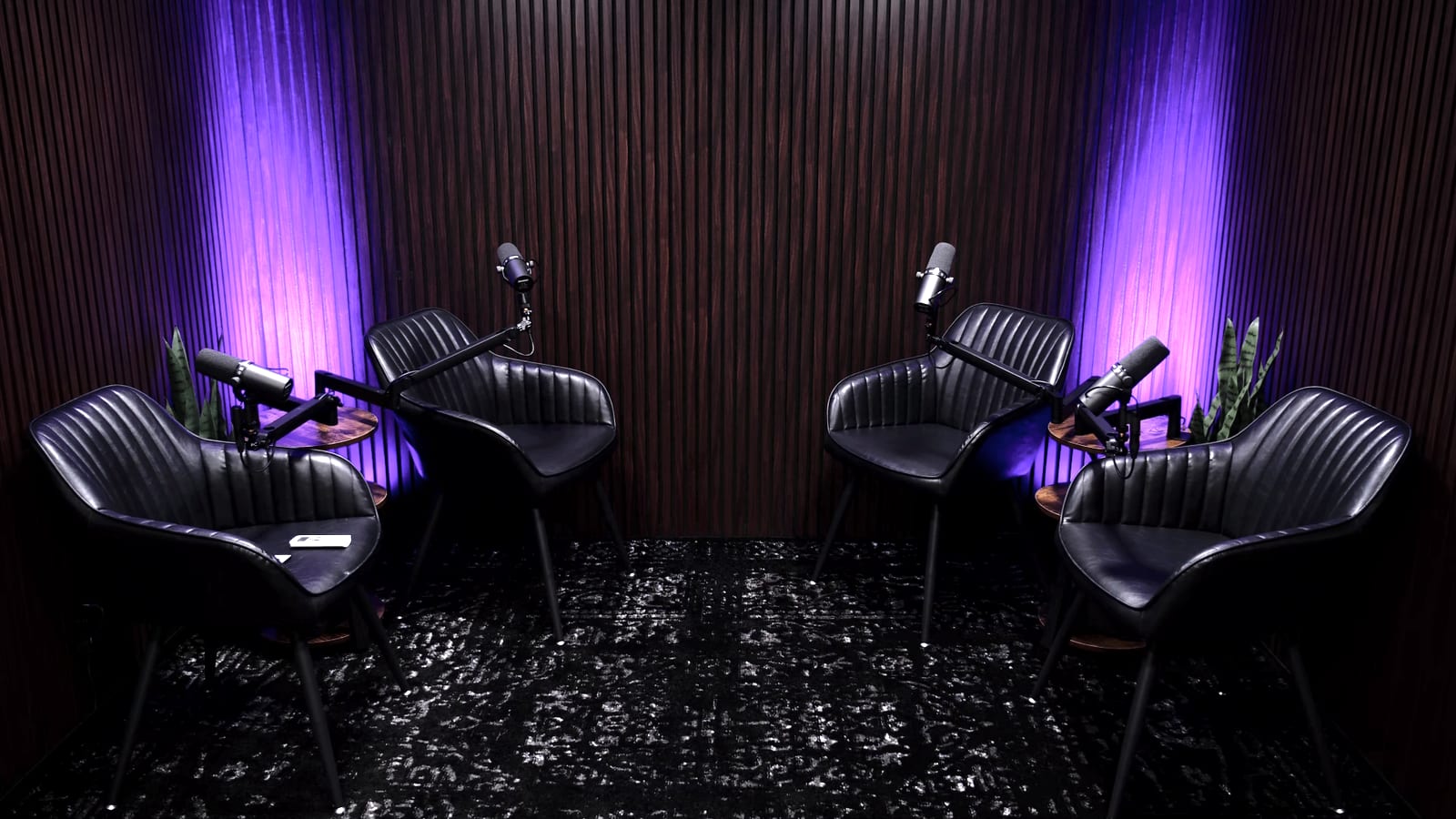 Poddy stüdyosu: ceviz akustik lata duvar önünde dört siyah deri koltuk ve dört mikrofon, mor RGB ışıkla aydınlatılmış